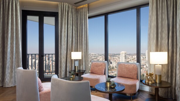 Une chambre d’hôtel moderne avec vue sur la ville, comprenant deux fauteuils, une table basse ronde et deux lampes.