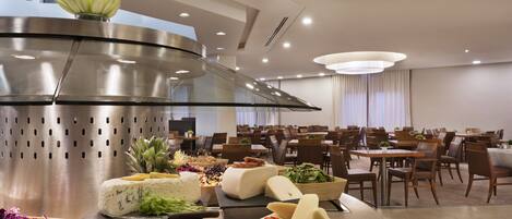 Un comedor moderno con una mesa buffet central, una campana extractora de acero inoxidable y un conjunto de mesas y sillas.
