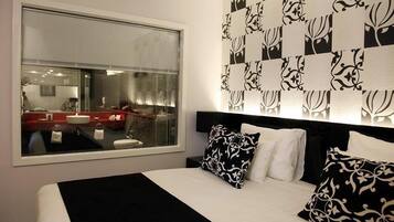 Habitació d'hotel moderna amb una finestra gran, un llit amb almoinos de disseny blanc i negre, i un mirall fixat a la paret.