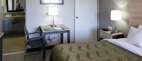 Habitación de hotel con cama, dos mesitas de noche con lámparas, un escritorio con silla, un espejo y una puerta.