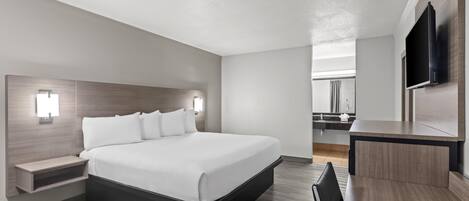 Une chambre d’hôtel moderne dotée d’un grand lit, de tables de chevet, d’un bureau et d’un téléviseur à écran plat fixé au mur.