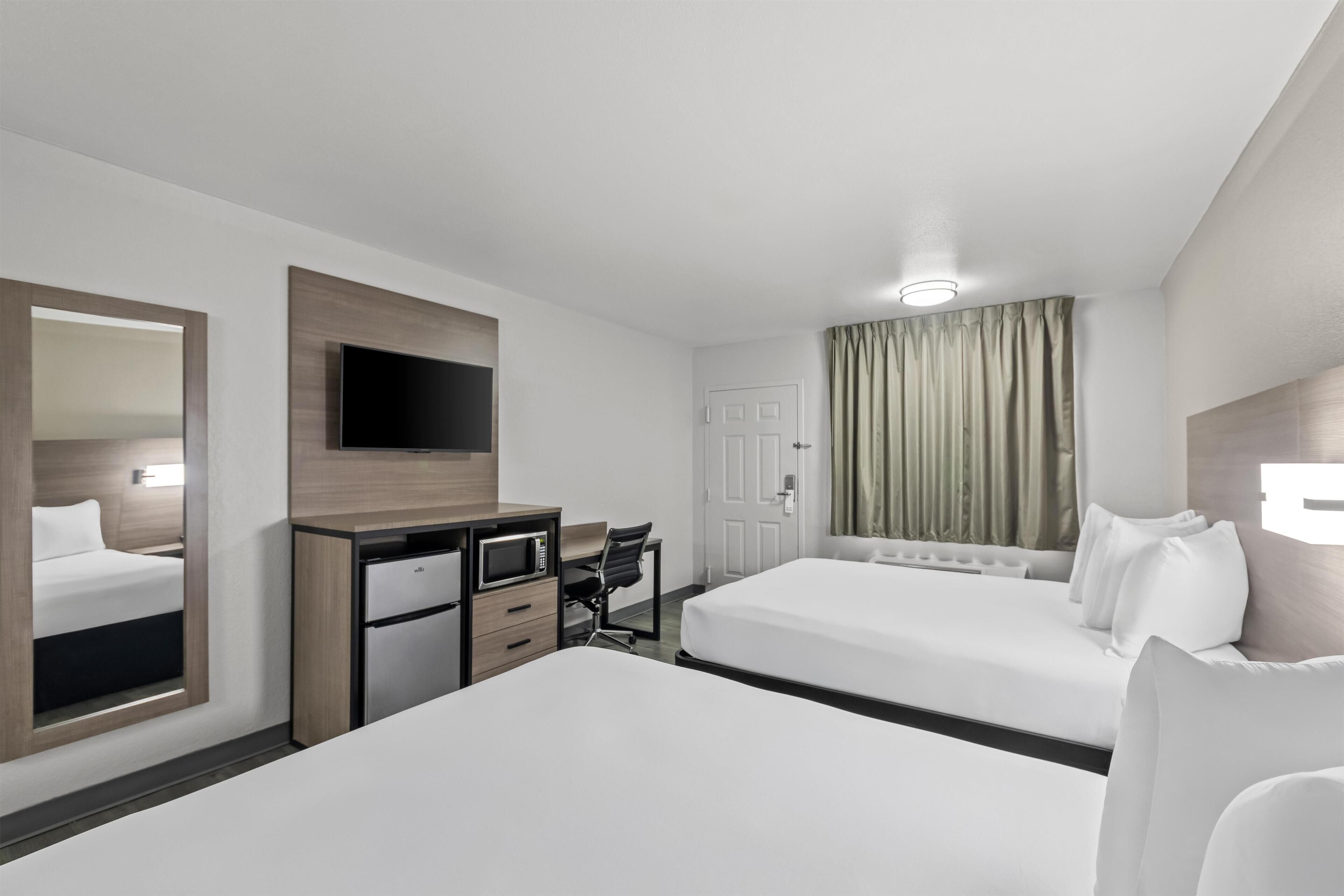 A hotel room with two beds, a desk, a chair, a TV, and a mirror.
