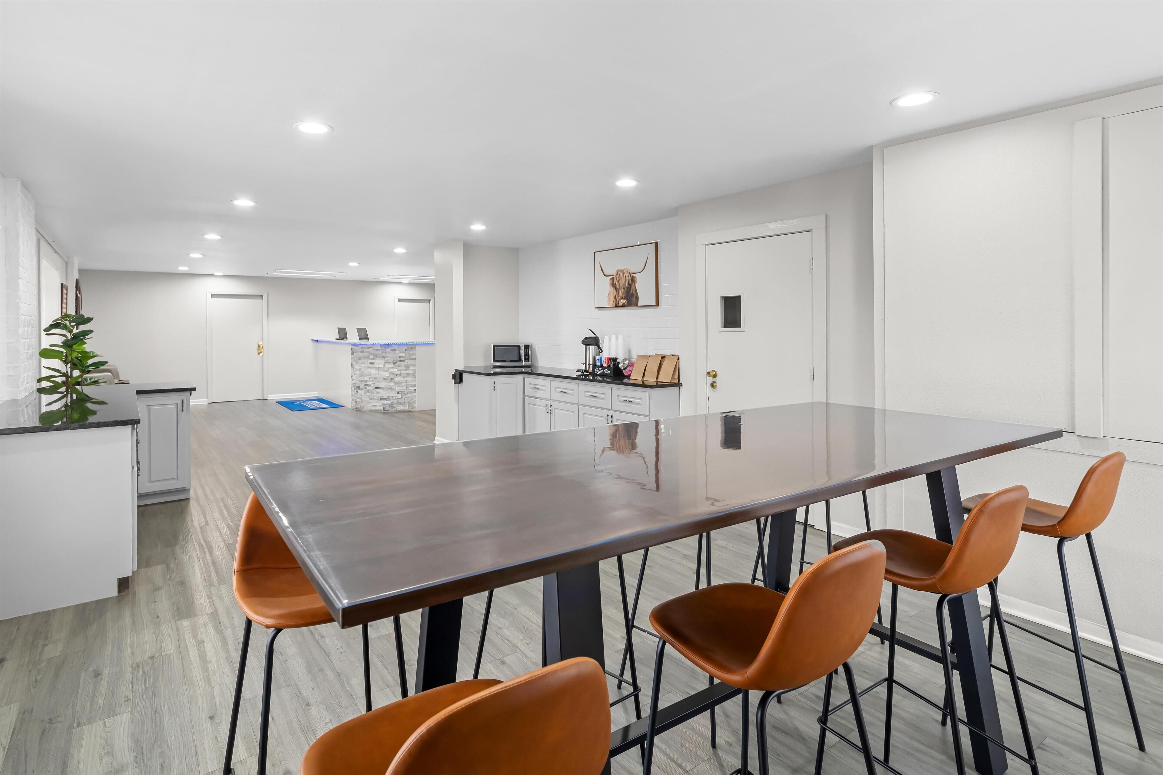 A modern kitchen with a central island, white cabinetry, and a large dining table with four chairs.
