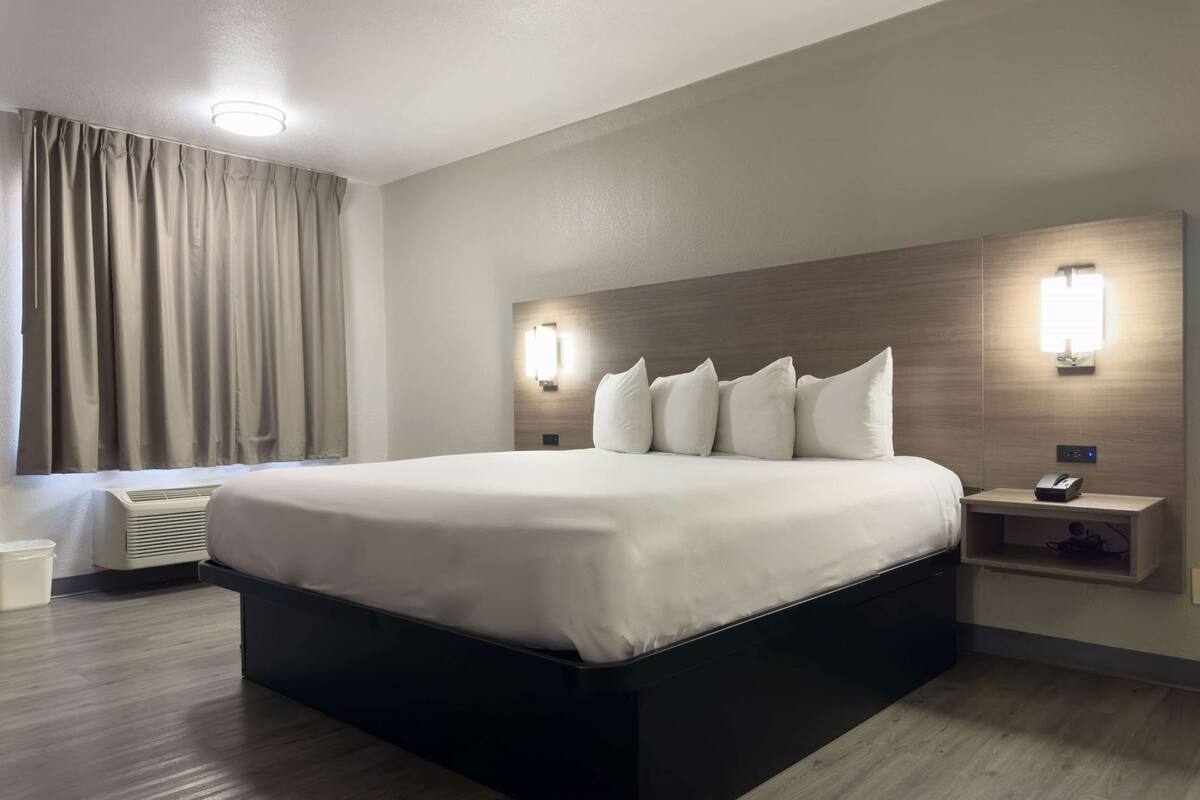 A modern hotel room with a large bed, bedside tables, a wall-mounted light, and a window with curtains.