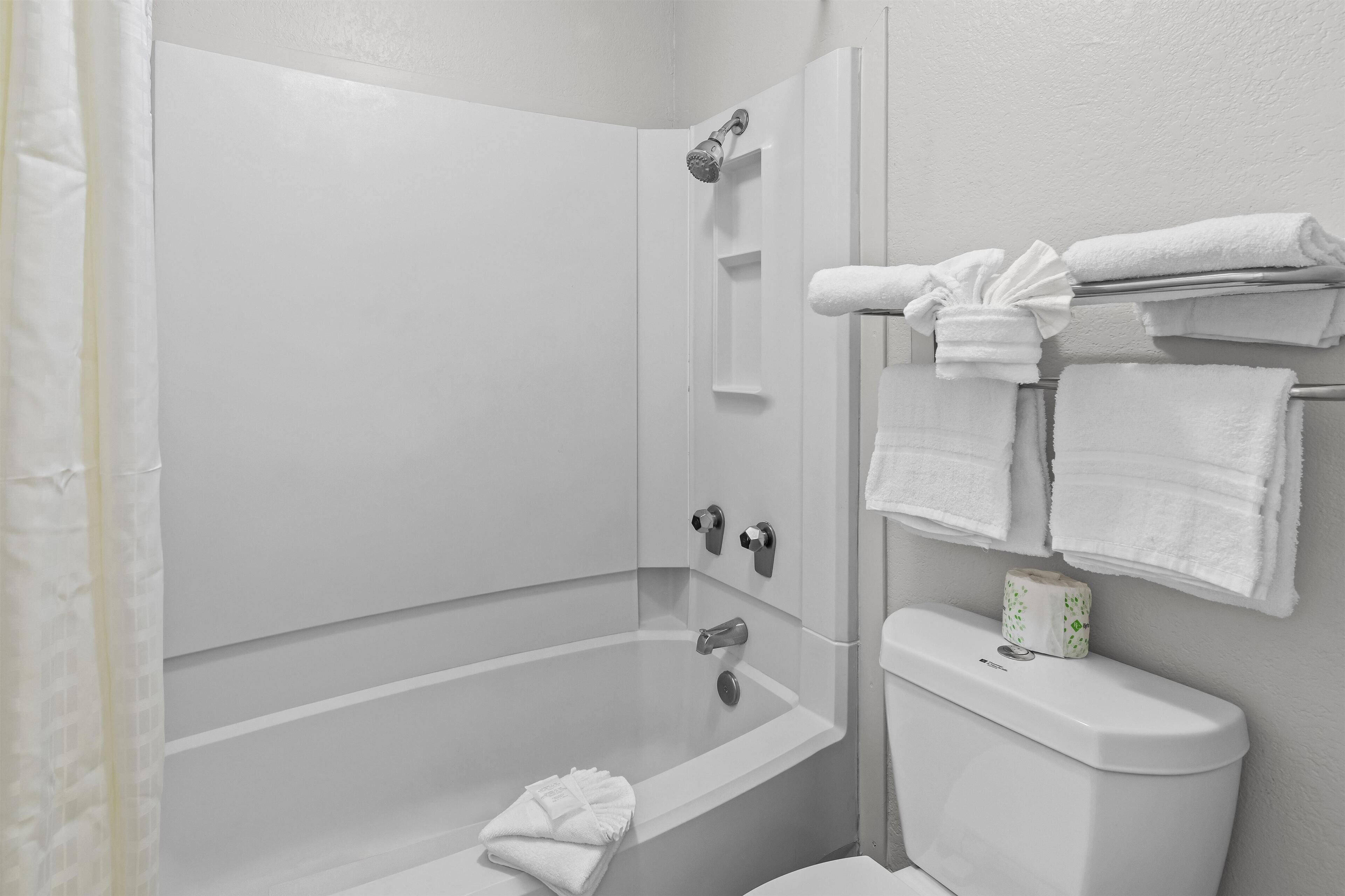 A bathroom with a bathtub, a toilet, and a shower. There are towels hanging on a rack and a toilet paper holder on the wall.