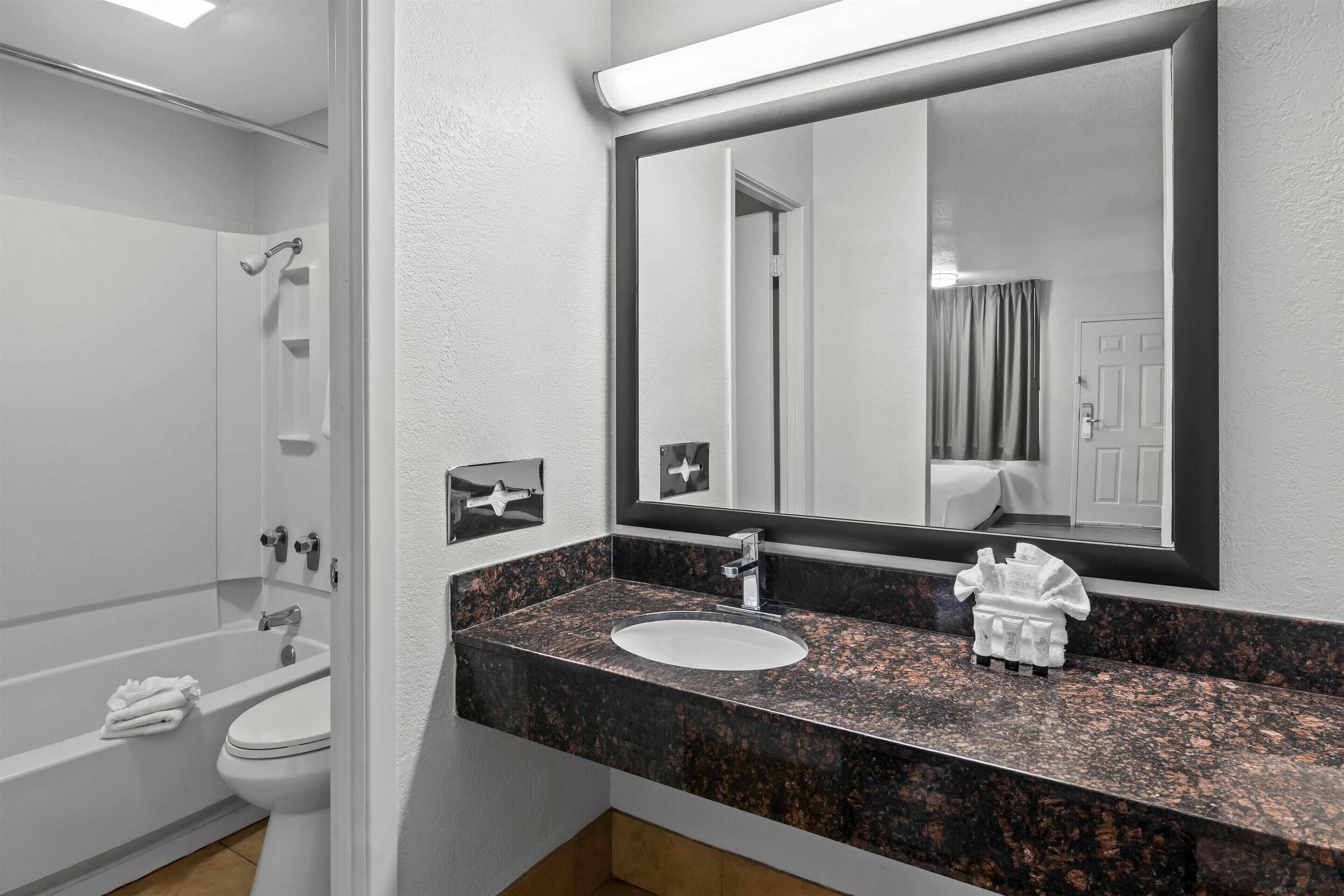 Un baño moderno con una bañera blanca, un lavabo con encimera de granito y un espejo grande sobre el lavabo.