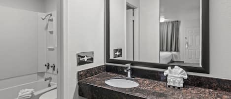 Un baño moderno con una bañera blanca, un lavabo con encimera de granito y un espejo grande sobre el lavabo.