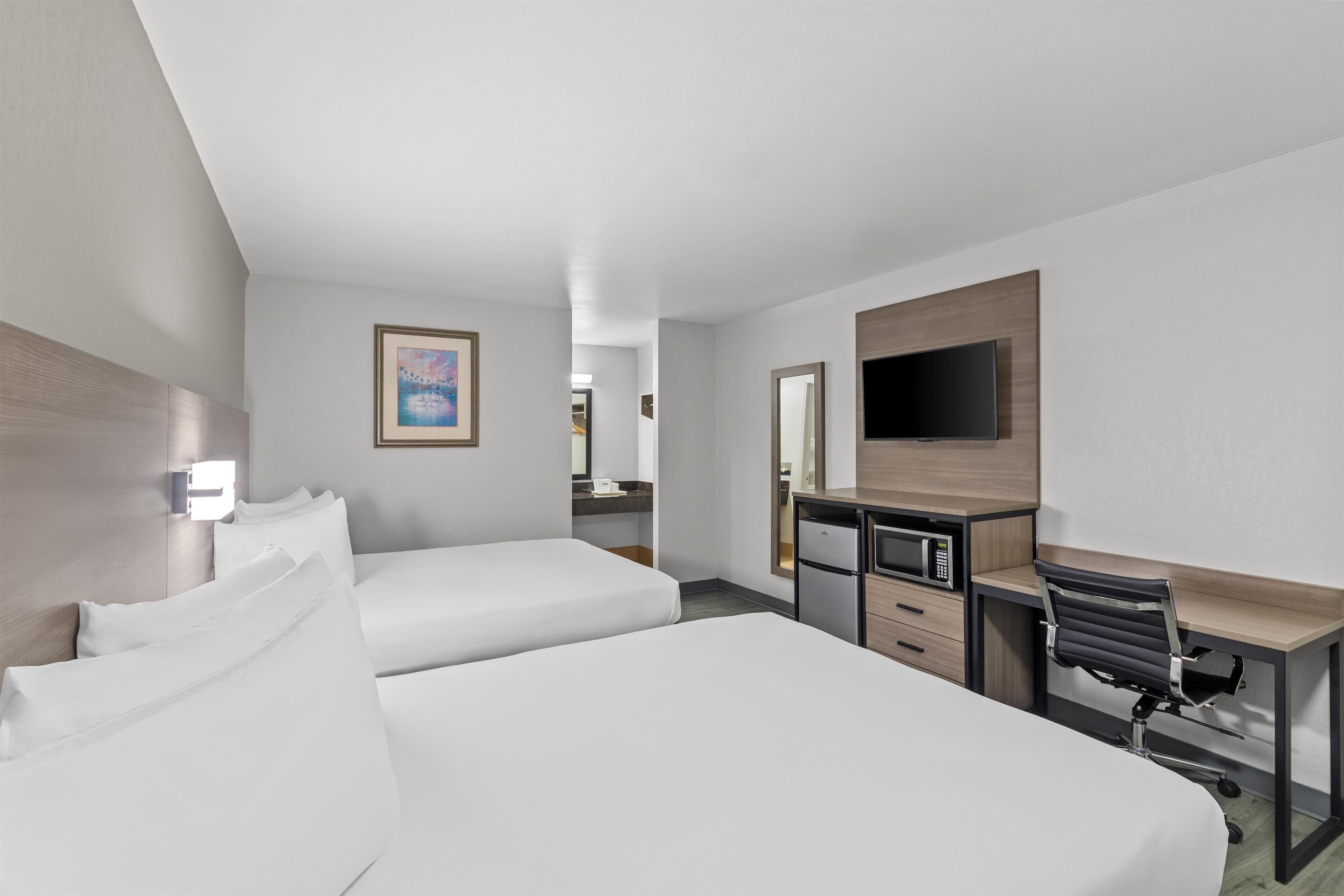 Habitación de hotel con dos camas, un escritorio, una silla, un televisor y una kitchenette pequeña.