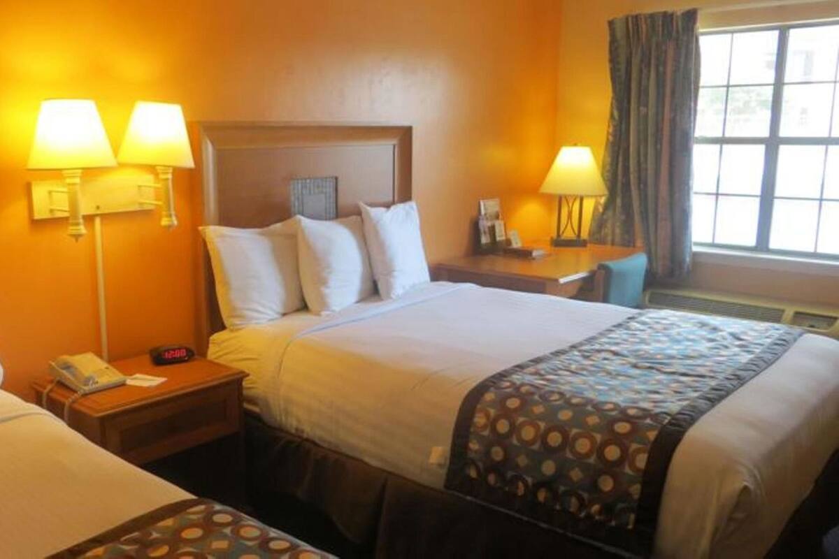 A hotel room with two beds, a nightstand with a phone and clock, and two wall-mounted lamps.