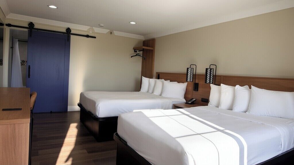 Habitación de hotel con dos camas, un escritorio, una puerta azul y un cabecero de madera.