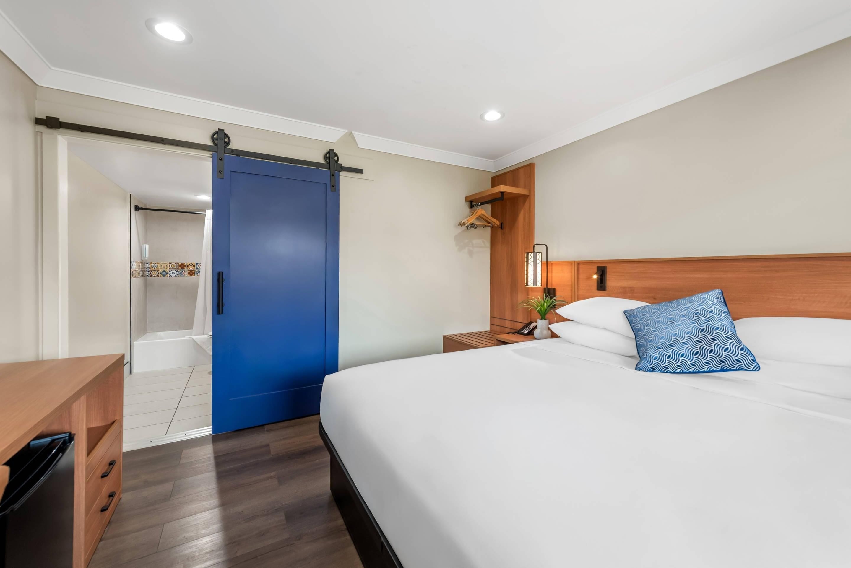 A hotel room with a large bed, a wooden nightstand, a blue sliding door, and a small bathroom visible through an open door.
