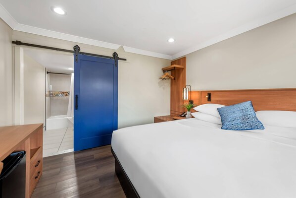 A hotel room with a large bed, a wooden nightstand, a blue sliding door, and a small bathroom visible through an open door.