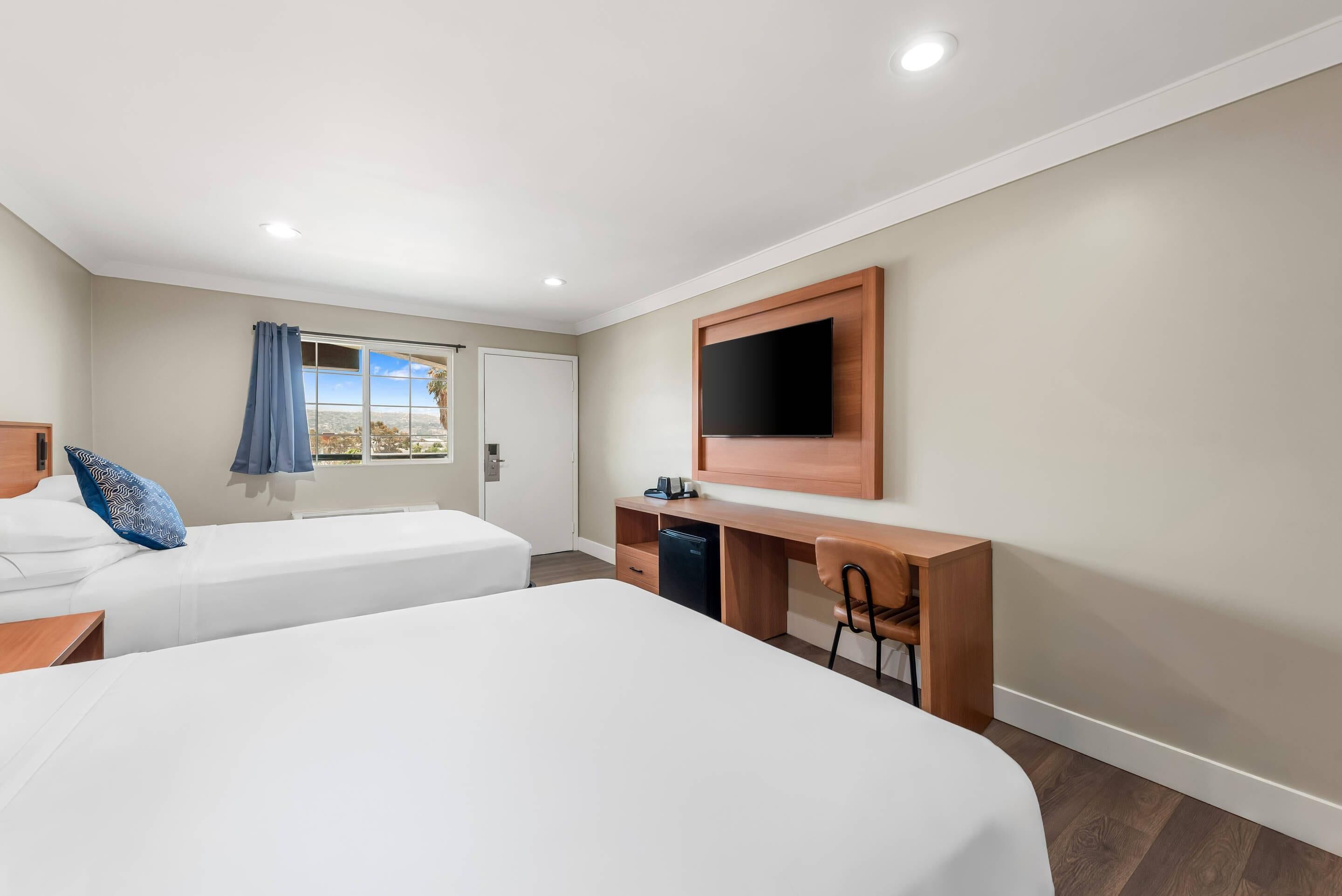 Habitación de hotel con dos camas, un escritorio, un televisor y una ventana con cortinas.
