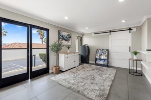 A modern interior with a large sliding door, a mounted abstract painting, a refrigerator, a magazine rack, and a small table with a plant.