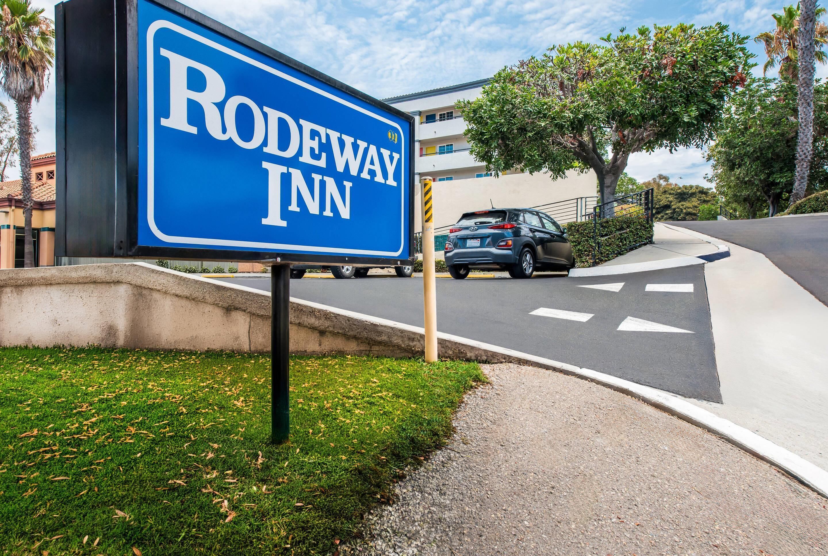 Skilt for Rodeway Inn med frit udsyn til vejen og en parkeret bil.