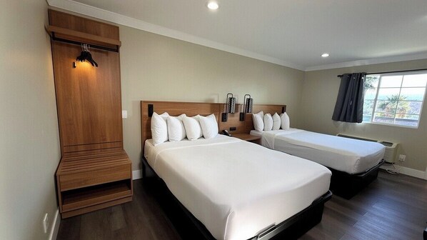 A hotel room with two beds, a wooden wardrobe, a bedside table, a wall-mounted lamp, and a window with curtains.