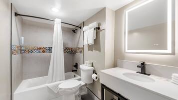 A bathroom with a shower, toilet, sink, and a mirror.