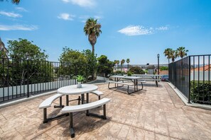 An outdoor patio area with round tables and benches, surrounded by a metal fence, palm trees, and a clear blue sky. - Rodeway Inn San Diego South San Ysidro Border (San Ysidro)