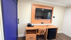 A compact room with a wooden desk, a chair, a small black trash bin, and a blue door.