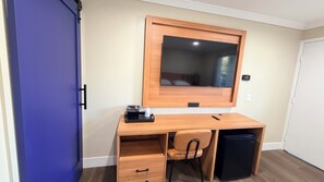 A compact room with a wooden desk, a chair, a small black trash bin, and a blue door.