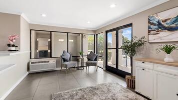 A modern living room with a large window, a fireplace, and a kitchen area.