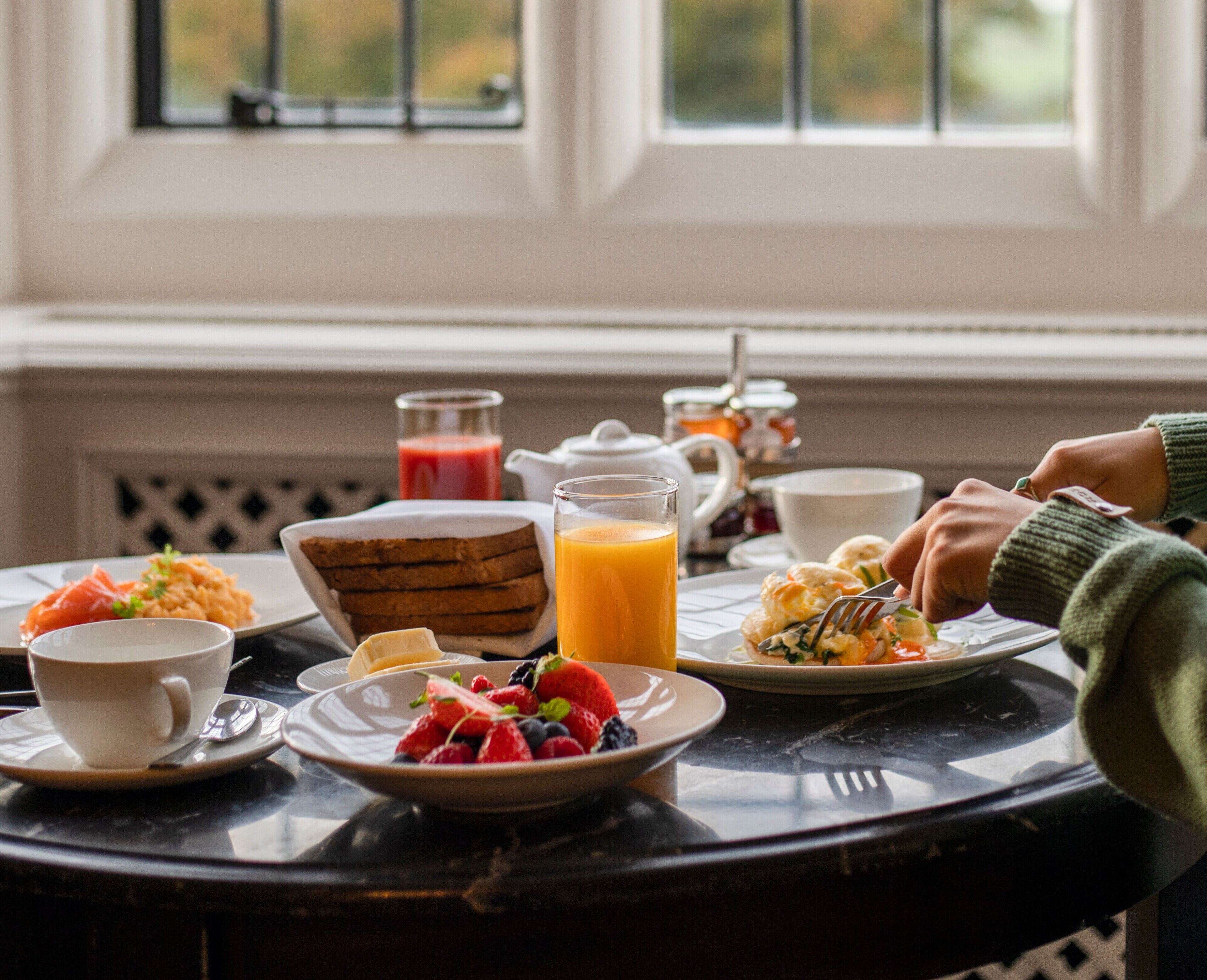 Un desayuno con diferentes platos, un vaso de jugo de naranja y vista a una ventana.