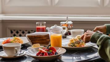 Un desayuno con diferentes platos, un vaso de jugo de naranja y vista a una ventana.