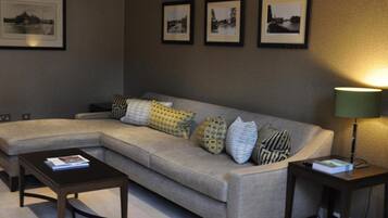 A living room with a sectional sofa, a coffee table, and a side table with a lamp. There are three framed pictures on the wall.