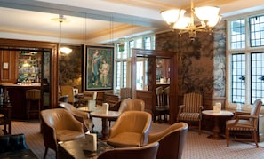 A traditional hotel lobby with leather armchairs, a bar area, and a large painting on the wall.
