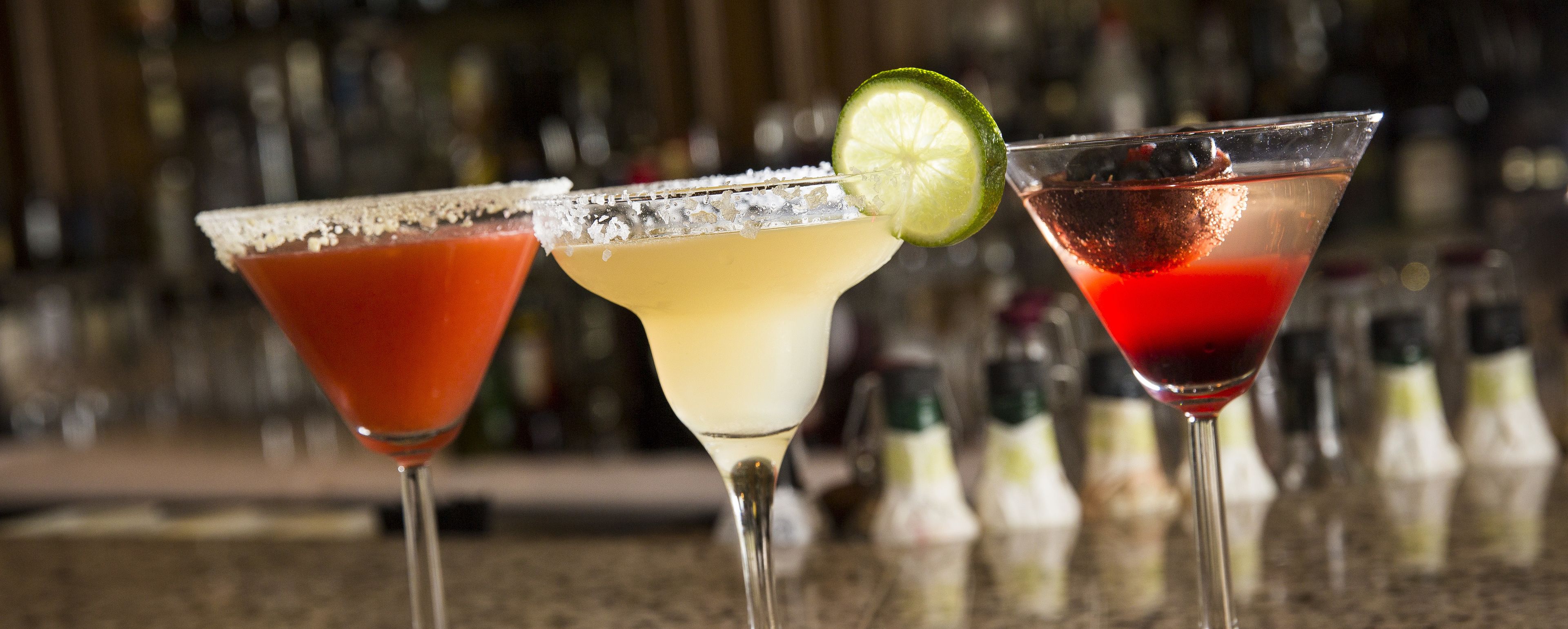 Three cocktails in martini glasses with lime garnishes.