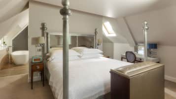 A bedroom with a large bed, a desk, a chair, a vanity with a mirror, and a skylight.