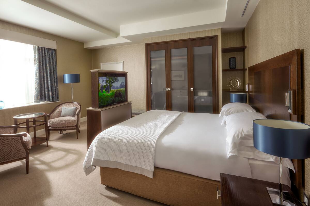 A hotel room with a large bed, a television, a desk, a chair, and a window with curtains.