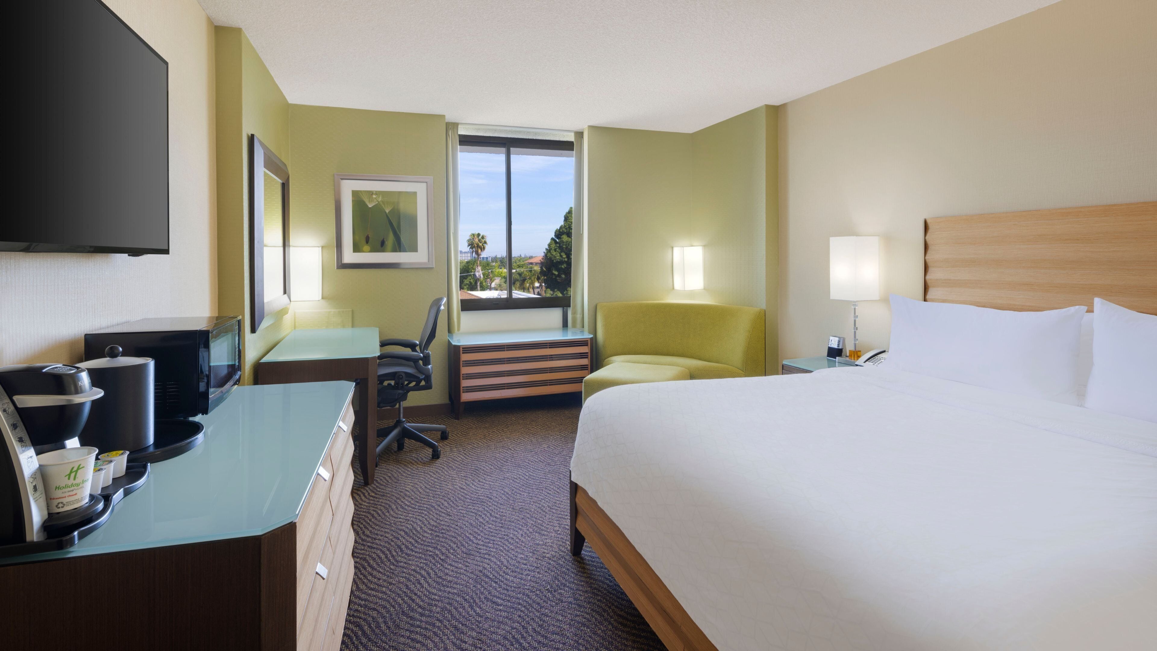 A hotel room with a bed, desk, chair, and a television.