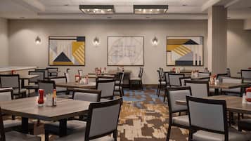 Un espace de restauration d'hôtel comprenant plusieurs tables et chaises, des œuvres d'art murales et un éclairage au plafond.