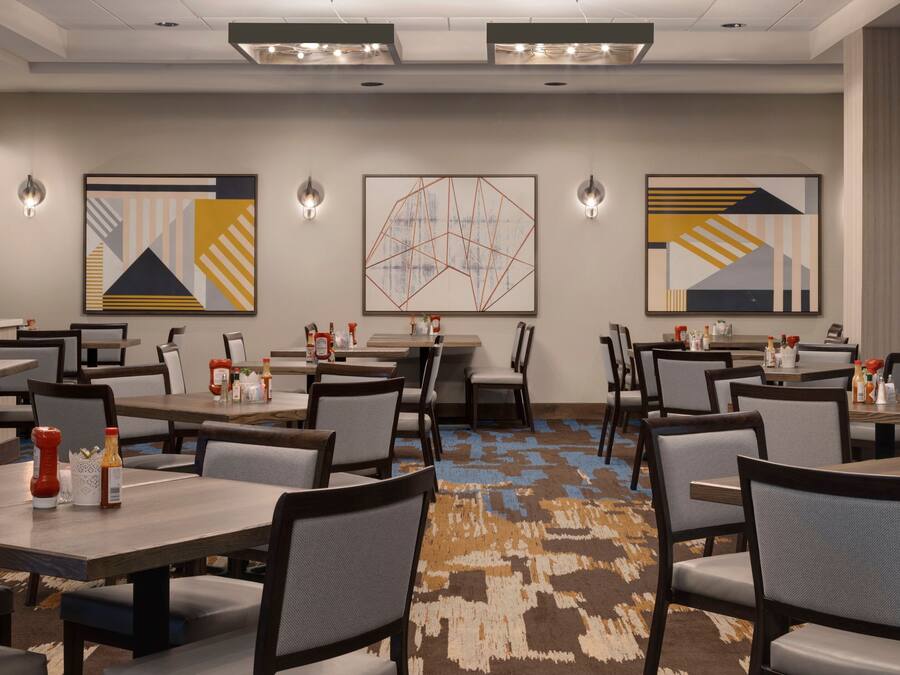Un espace de restauration d'hôtel comprenant plusieurs tables et chaises, des œuvres d'art murales et un éclairage au plafond.
