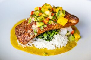 Un piatto con un filetto di pesce, riso e salsa gialla.