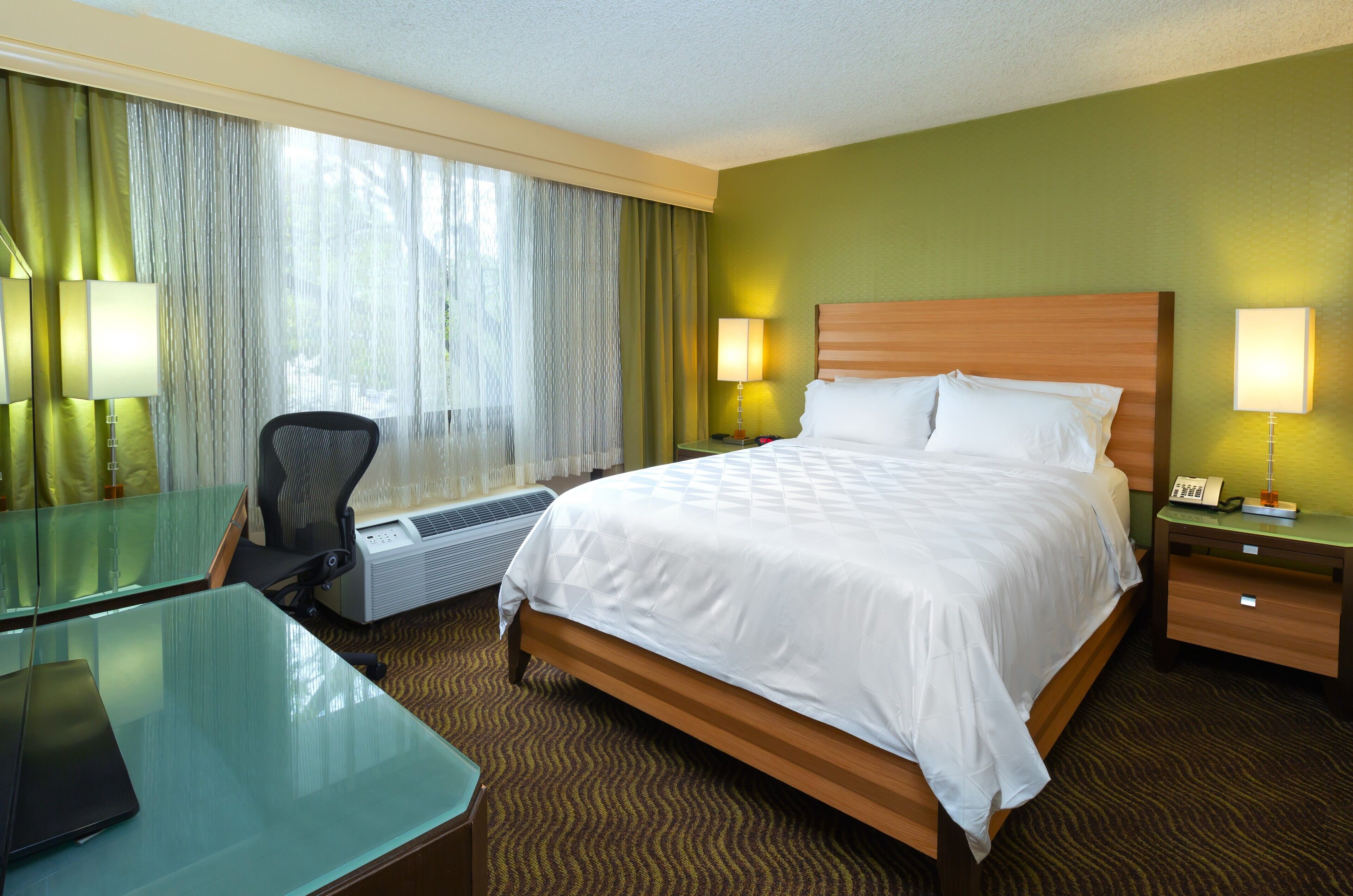 A hotel room with a bed, desk, chair, and a telephone on a nightstand.