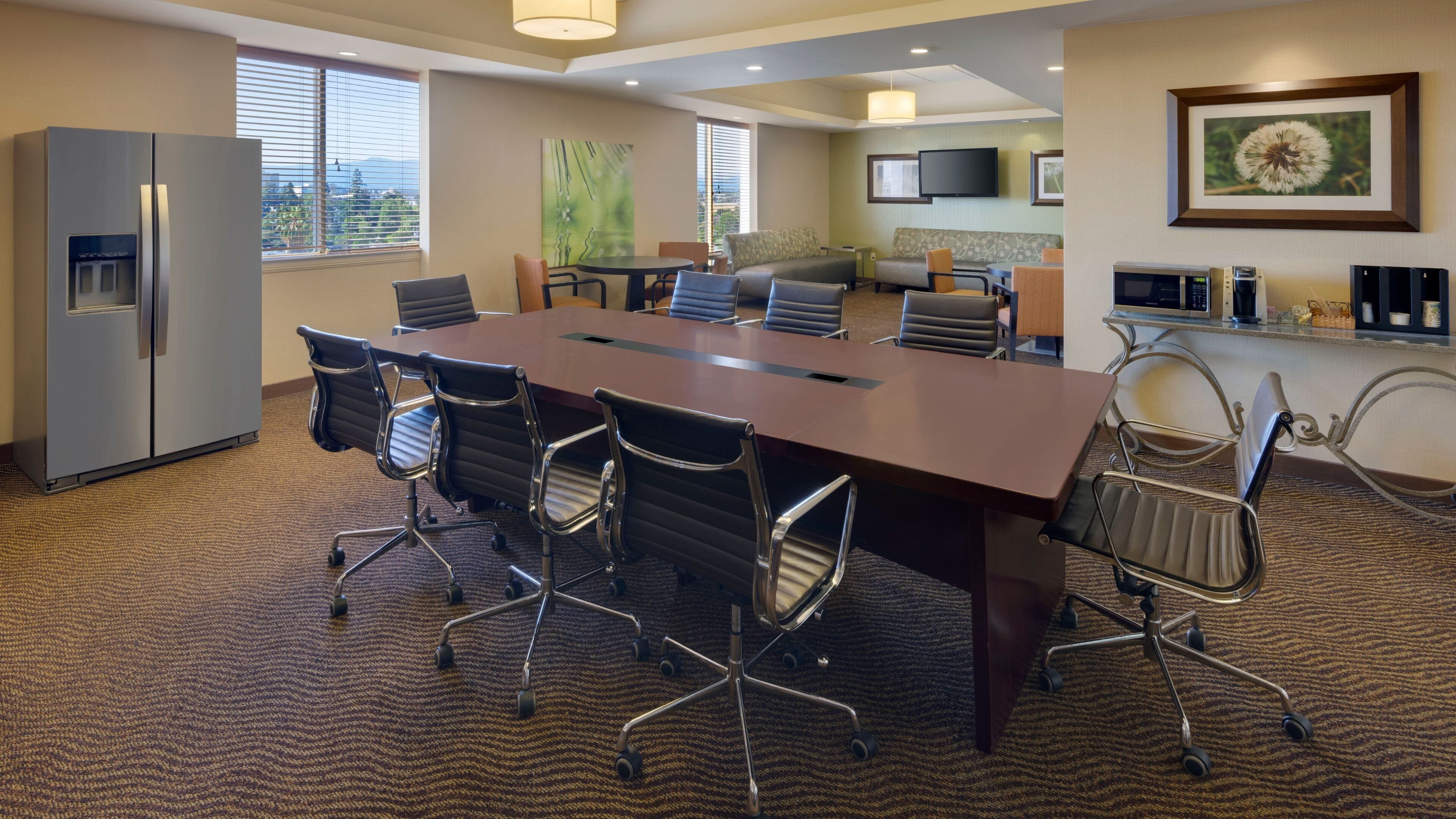 A conference room with a large table, chairs, a refrigerator, a television, and a framed picture on the wall.