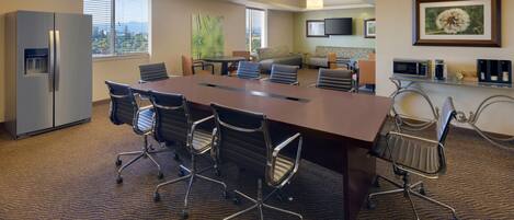 A conference room with a large table, chairs, a refrigerator, a television, and a framed picture on the wall.