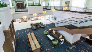 A spacious lobby with a high ceiling, a central seating area with sofas and chairs, a long wooden table, and a staircase leading to an upper level. - Holiday Inn San Jose - Silicon Valley by IHG (San Jose)