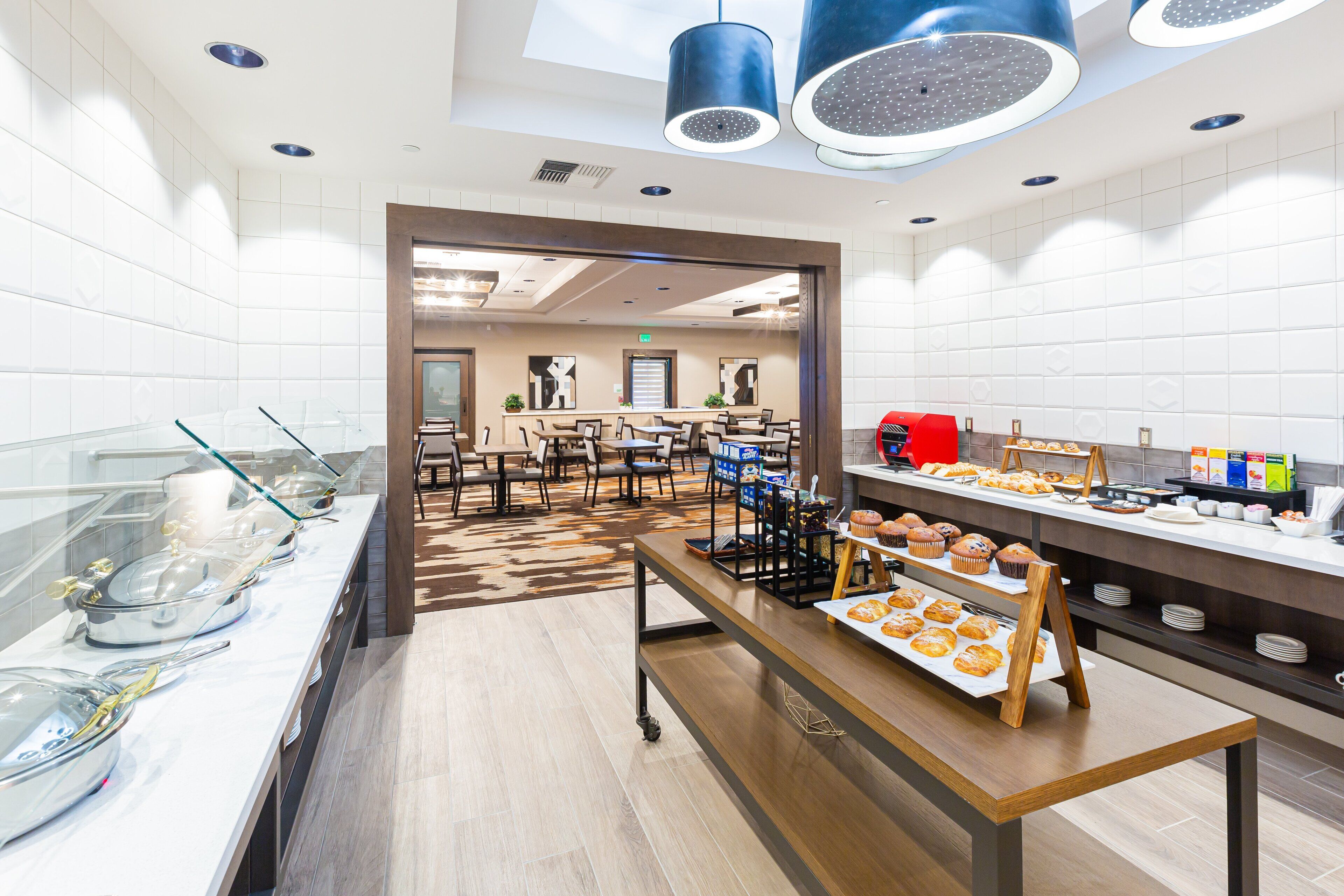 Ein moderner Frühstücksbereich mit Buffet, darunter eine Auswahl an Gebäck und eine Selbstbedienungsstation.