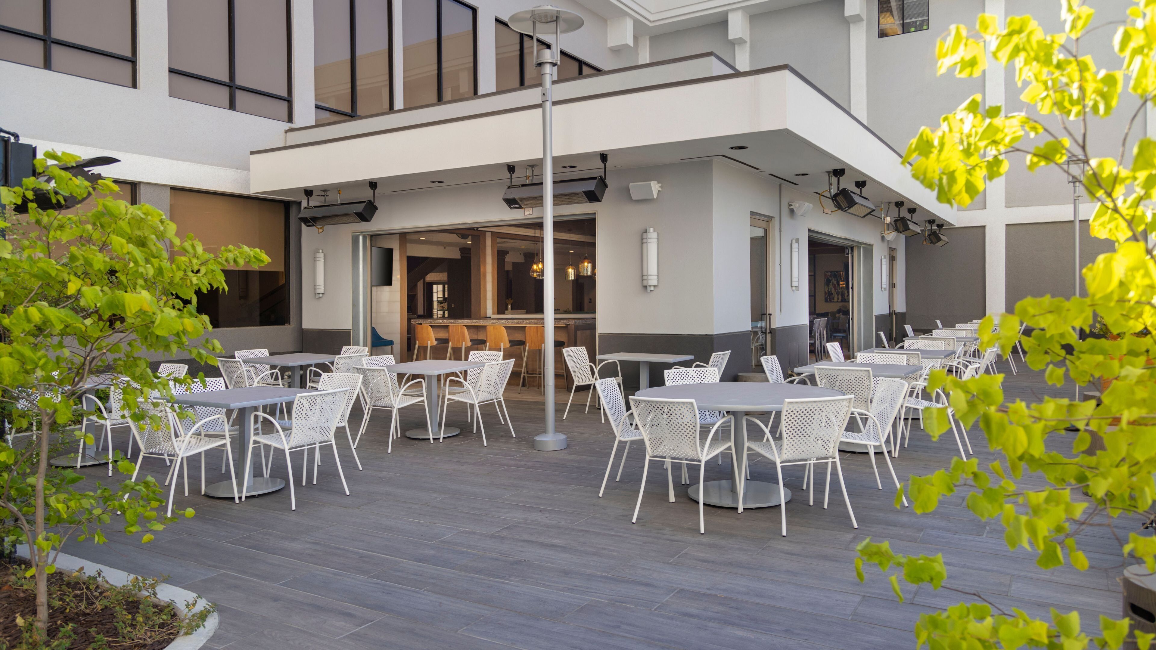 An outdoor seating area with tables and chairs, a bar, and a building with large windows.