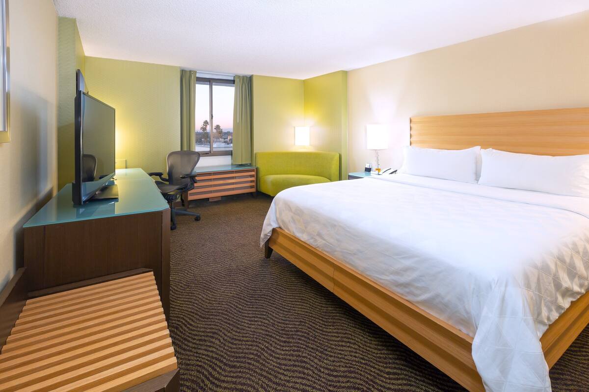 A hotel room with a bed, a desk with a computer, a chair, and a TV.