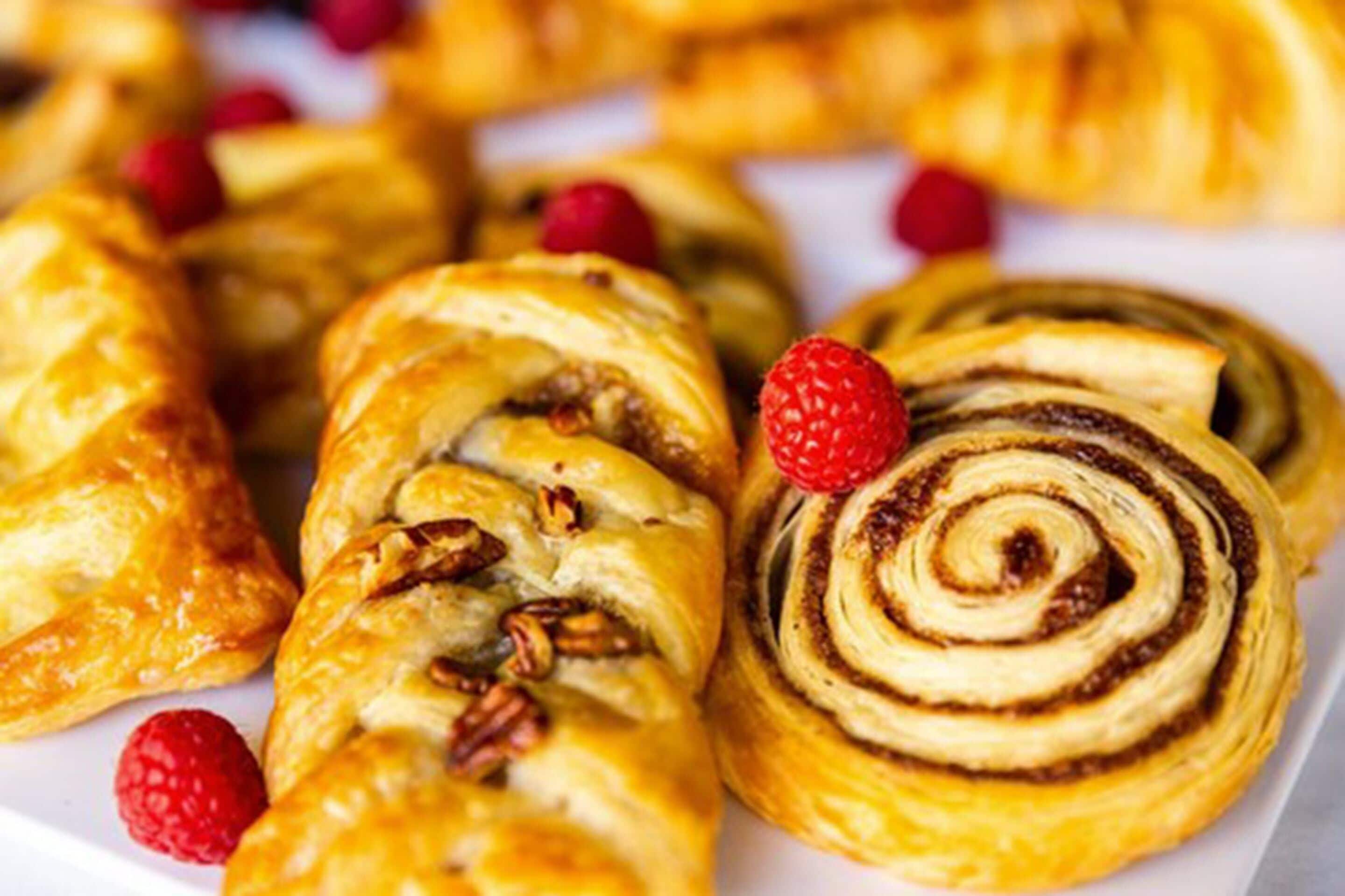 Variedad de pasteles, incluyendo un rollo de canela y pasteles con nueces pecanas, dispuestos en un plato con frambuesas.