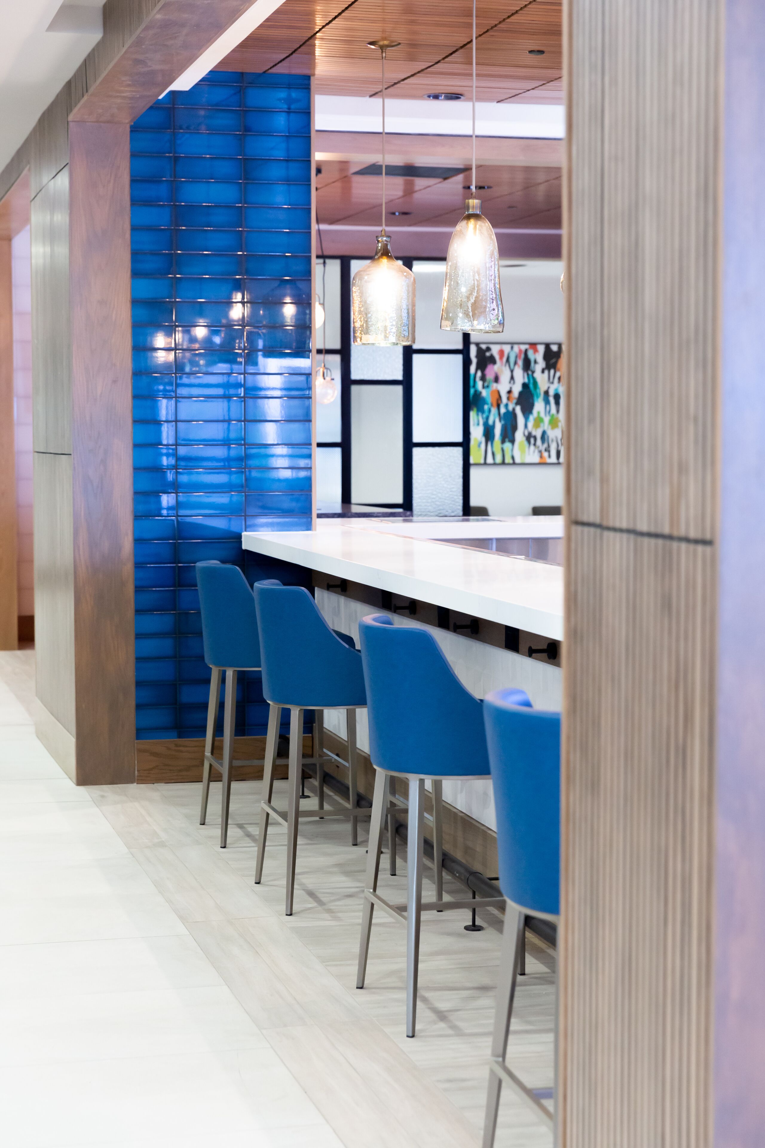 A modern bar area with a long counter, blue bar stools, and pendant lighting.