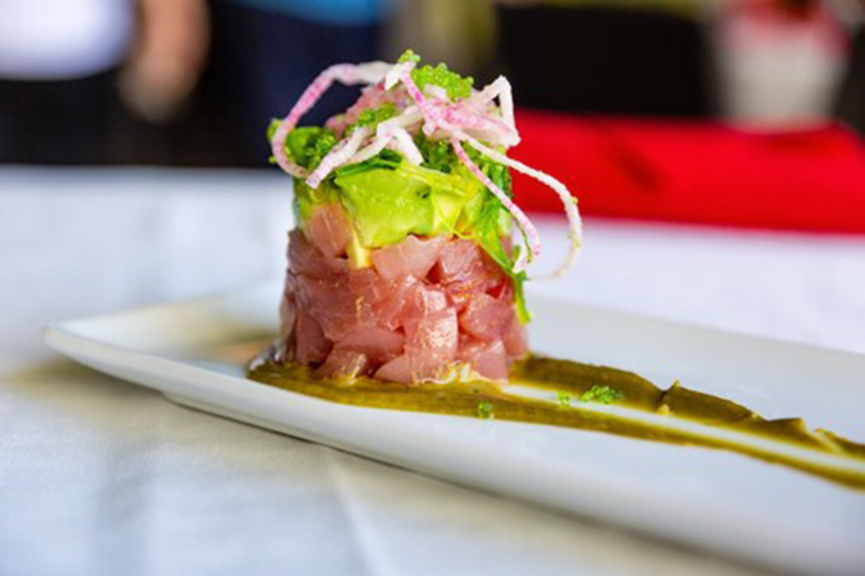 A dish of raw fish on a white plate with a green sauce and shredded vegetables.
