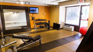 Ein Fitnessraum mit Trainingsgeräten, einem Fernseher und einem Notausgang.