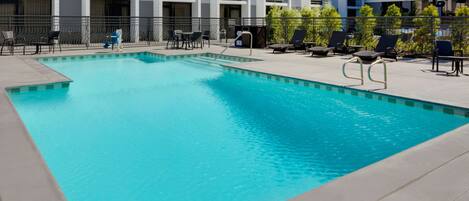 A rectangular swimming pool with a metal ladder, surrounded by lounge chairs and tables.