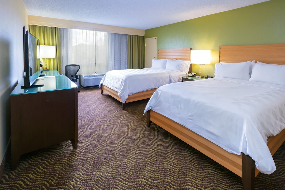 A hotel room with two beds, a desk with a TV, a chair, and a desk lamp.
