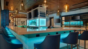 A modern bar area with a long counter, bar stools, and pendant lighting. - Holiday Inn San Jose - Silicon Valley by IHG (San Jose)